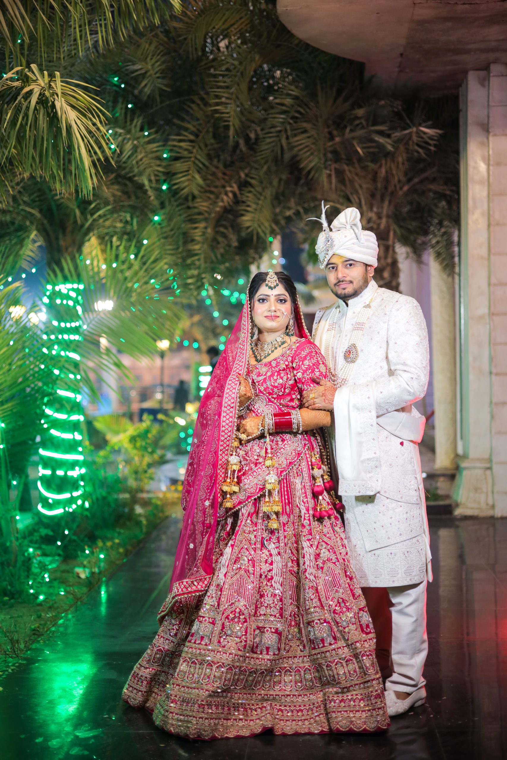 Groom in a white sherwani standing beside his partner in a pink wedding outfit