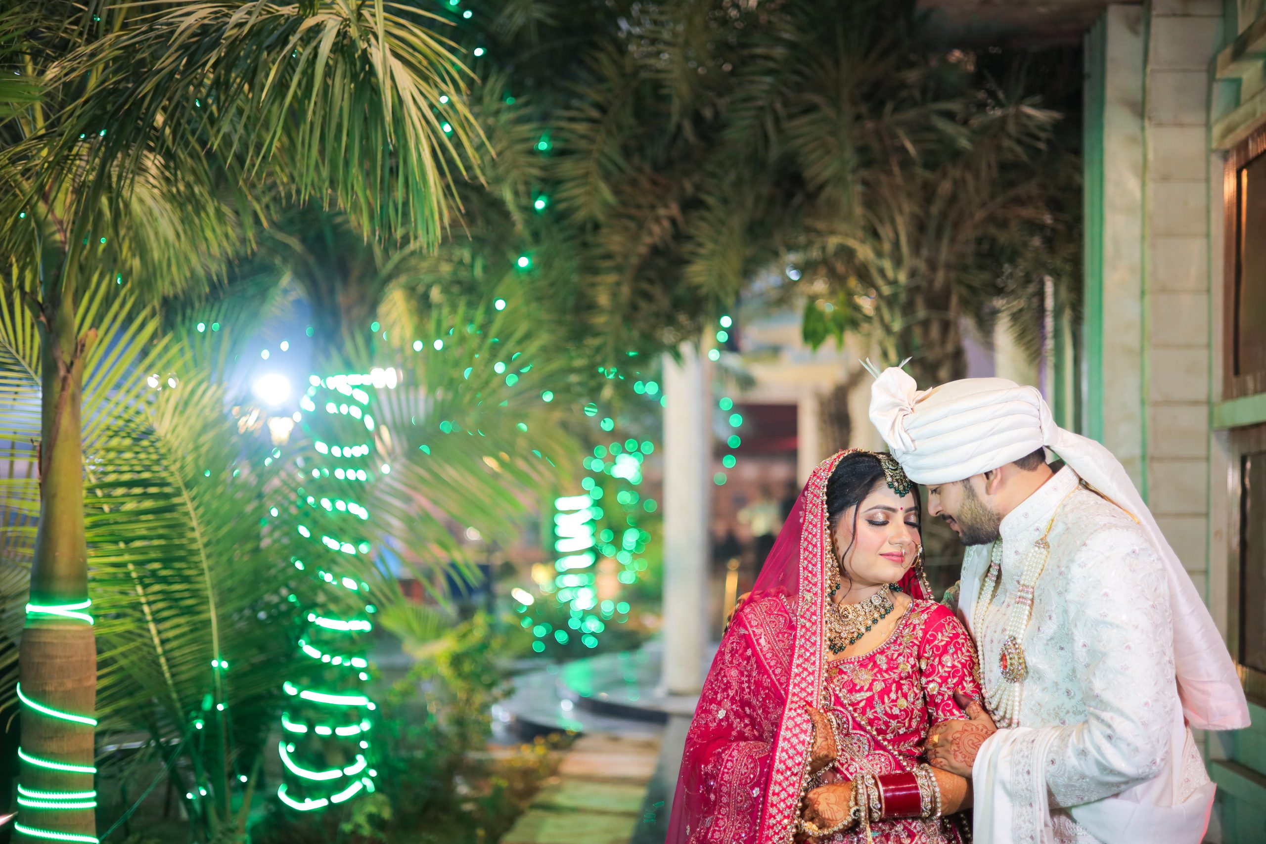 Indian wedding couple standing together in a garden with decorative greenery