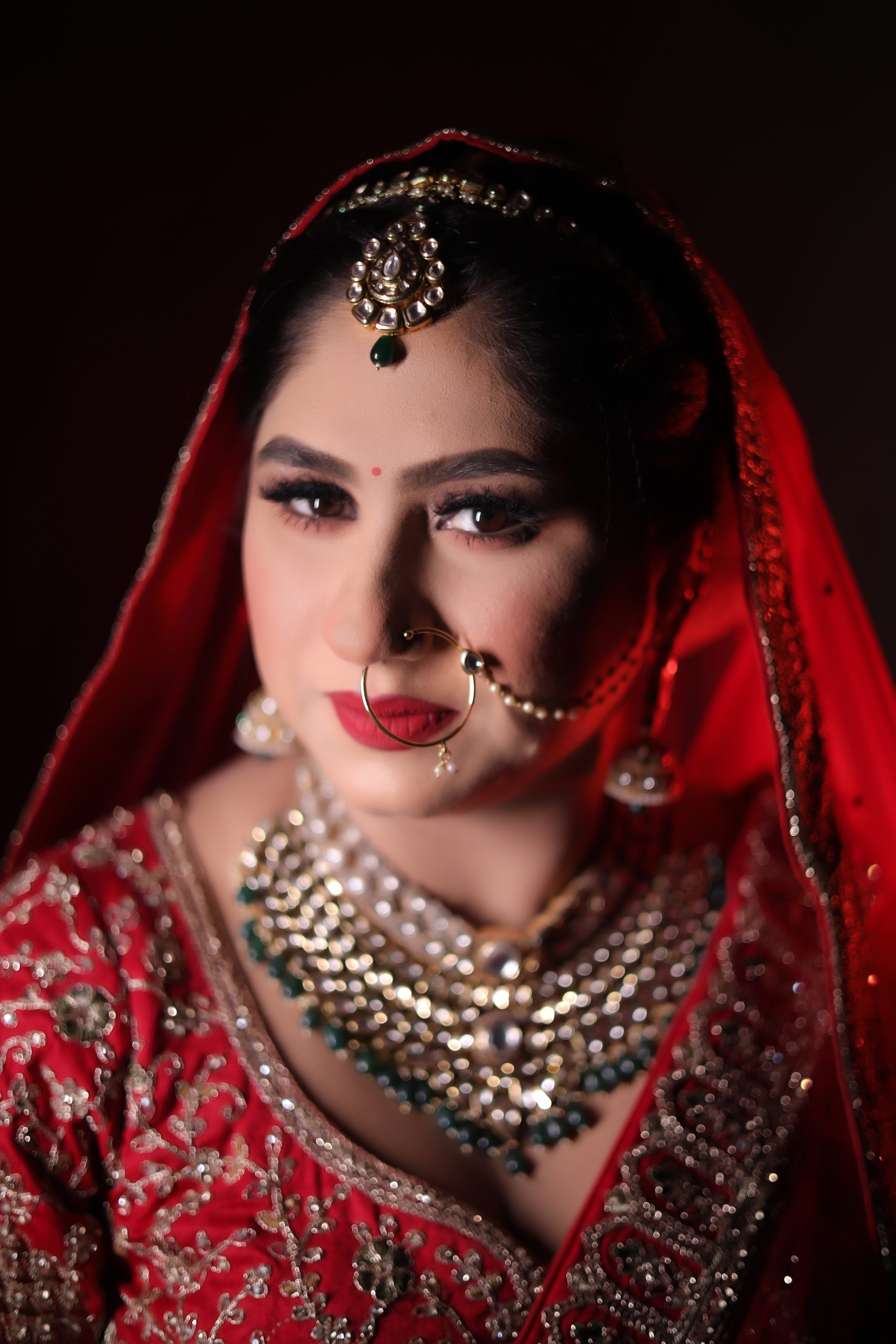 Close-up portrait featuring a red veil, nose ring and gold wedding jewelry