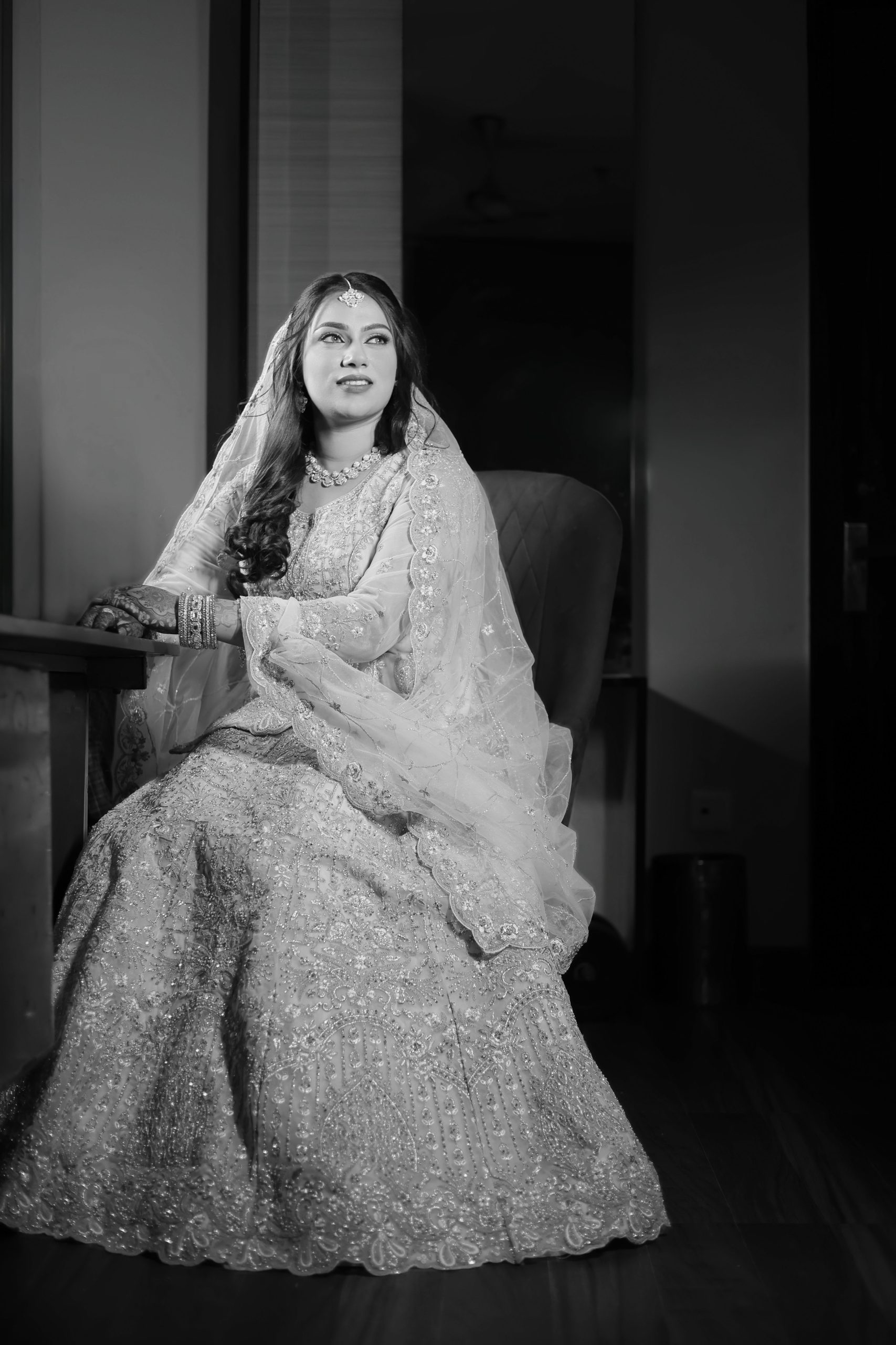 Woman seated in a light-colored wedding outfit for a black and white portrait