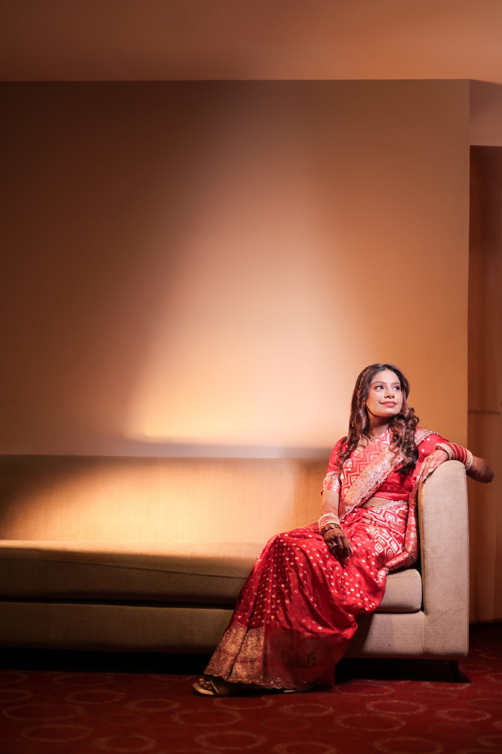 Bride standing alone in a red lehenga under warm lighting