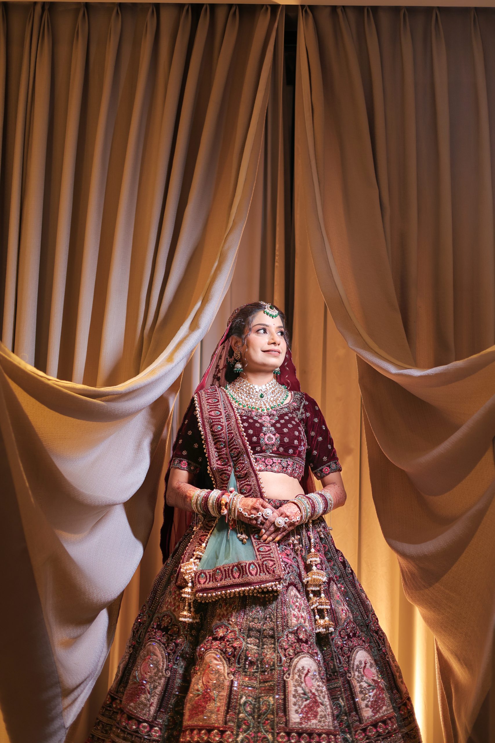 Bride seated in a red bridal outfit against golden curtains