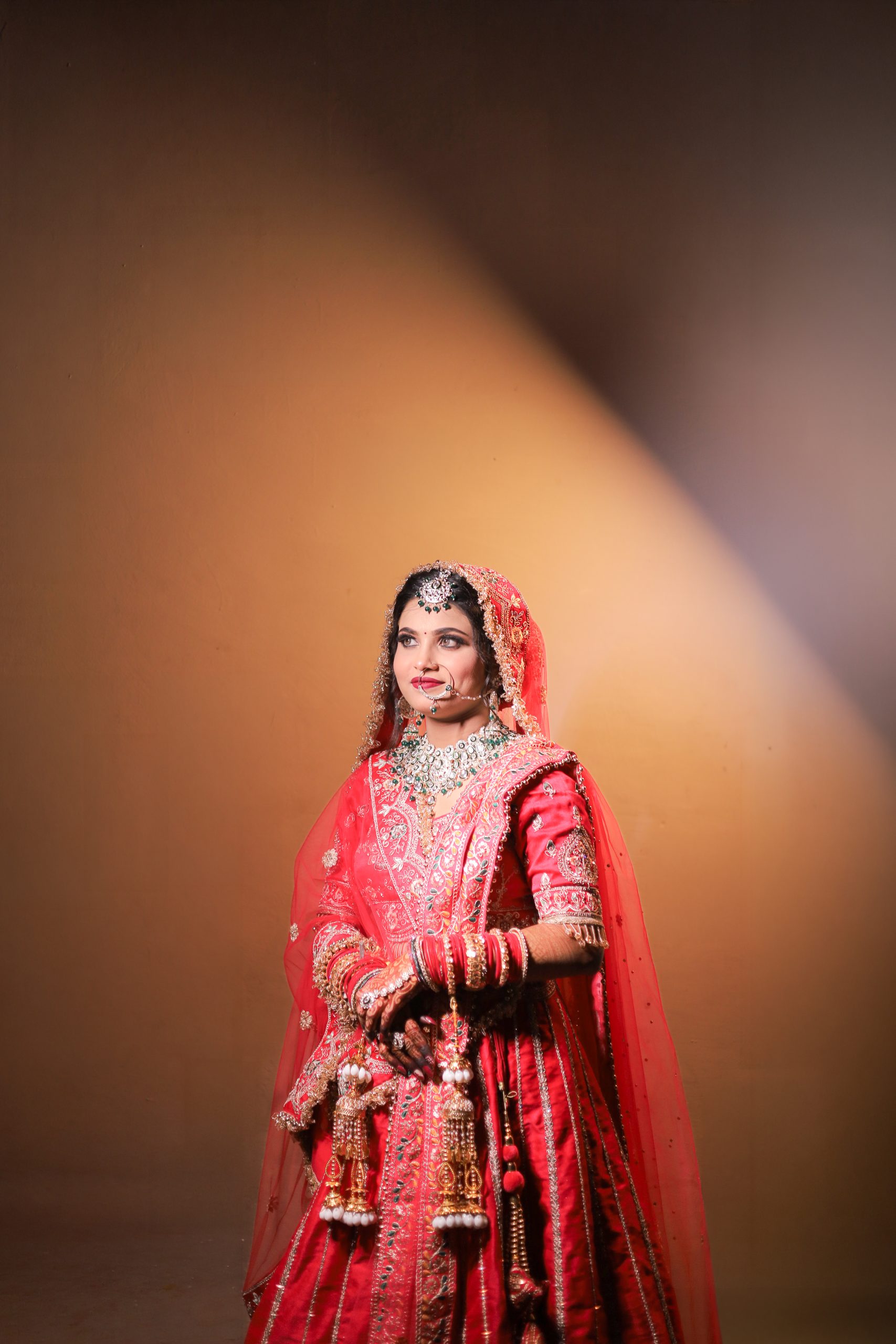 Bride standing in a red lehenga against a warm spotlight