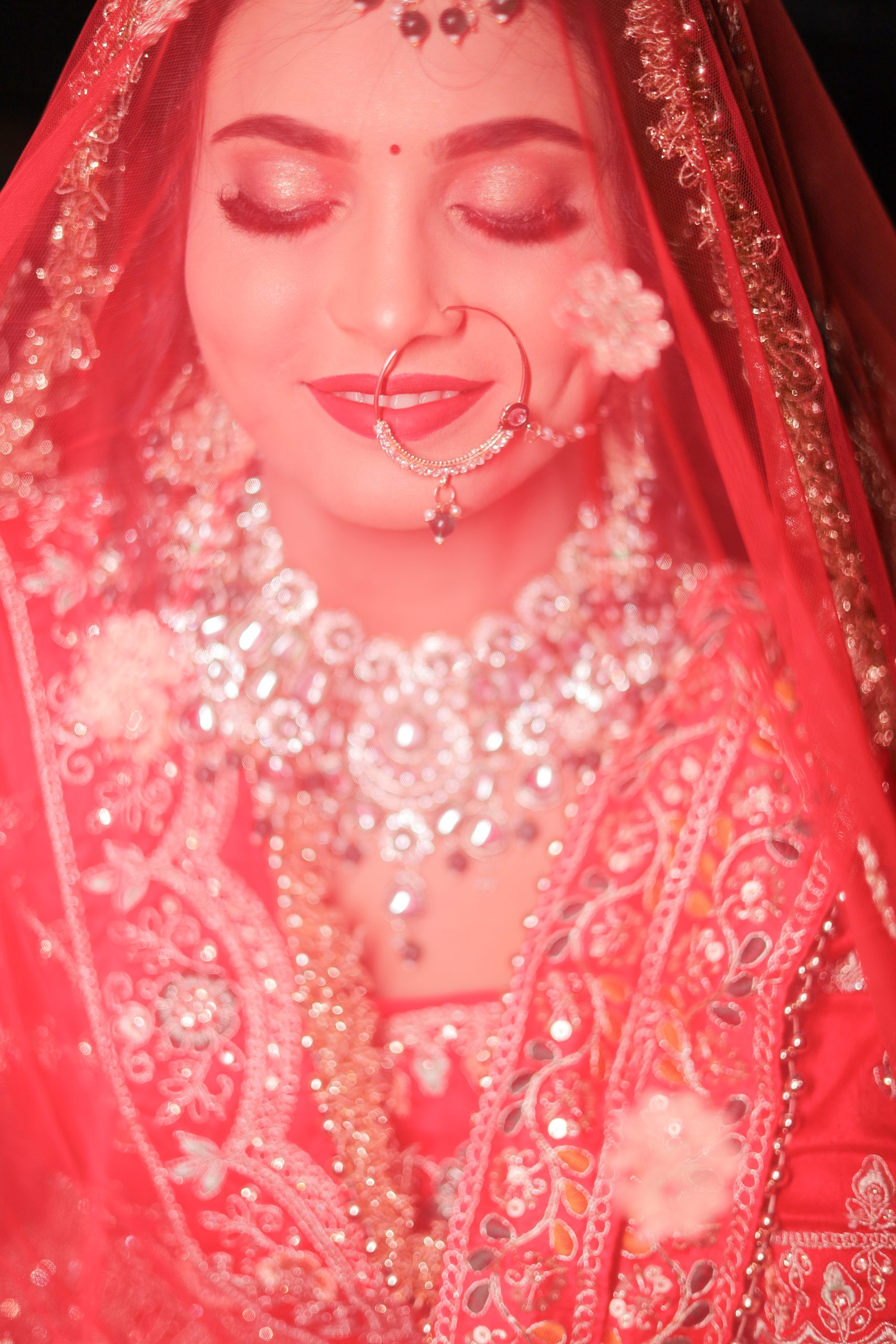 Close-up bridal photograph highlighting a red veil and wedding jewelry