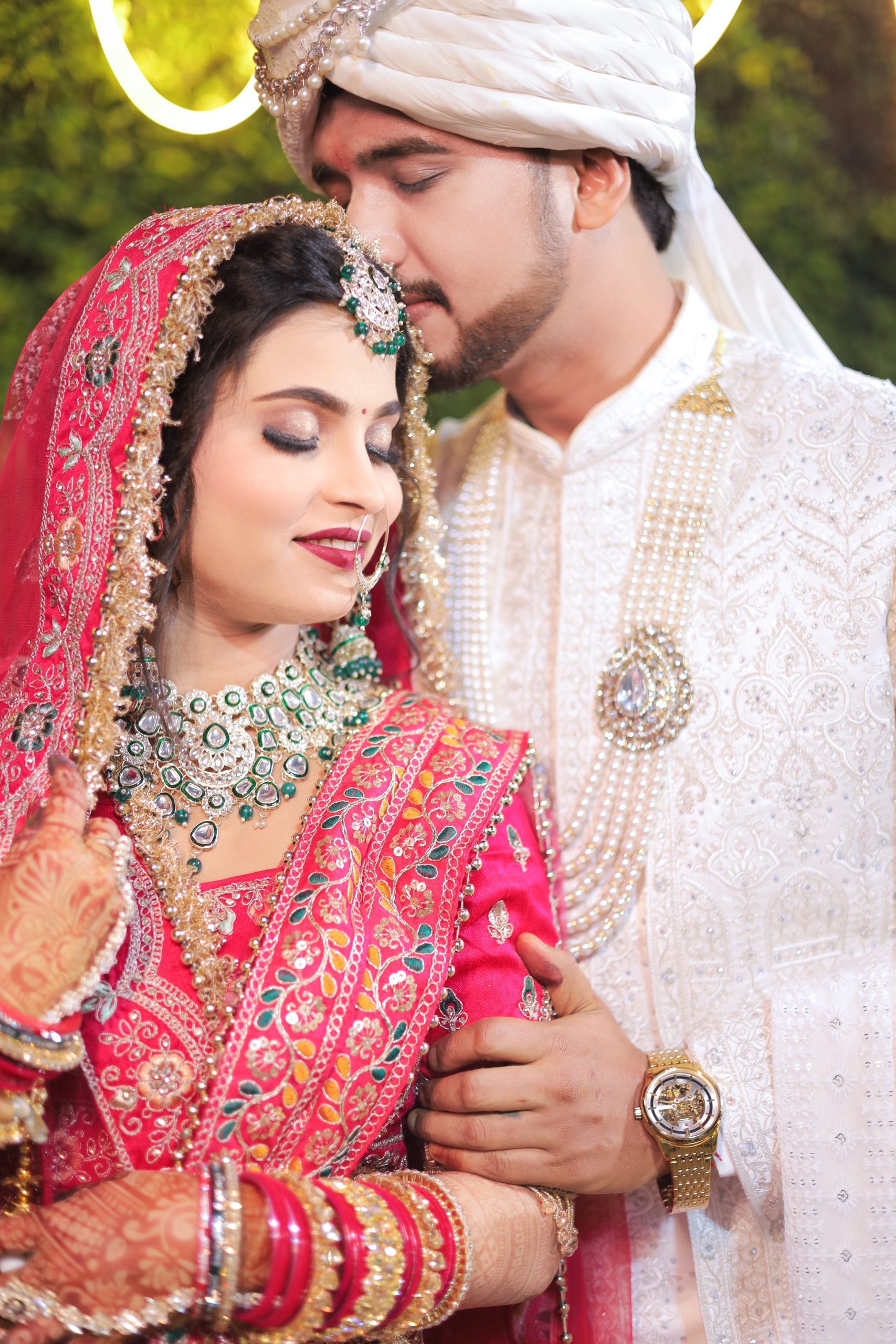 Bride in a red bridal lehenga posing closely beside the groom