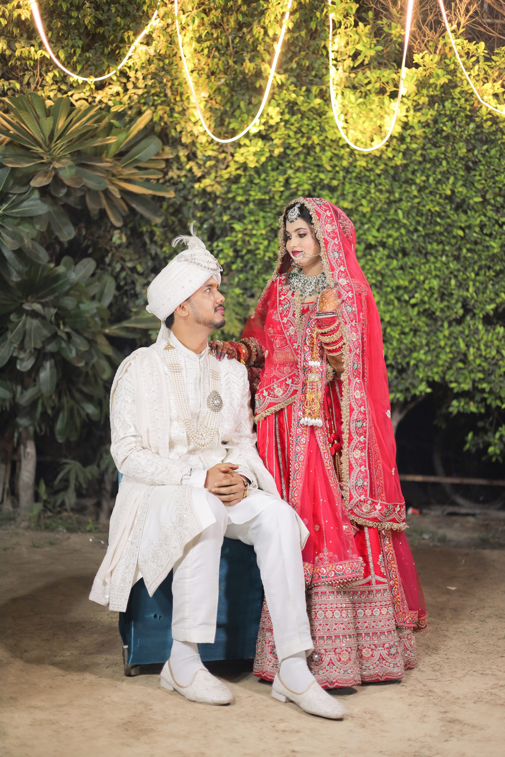 Bride in a red lehenga standing beside the groom outdoors